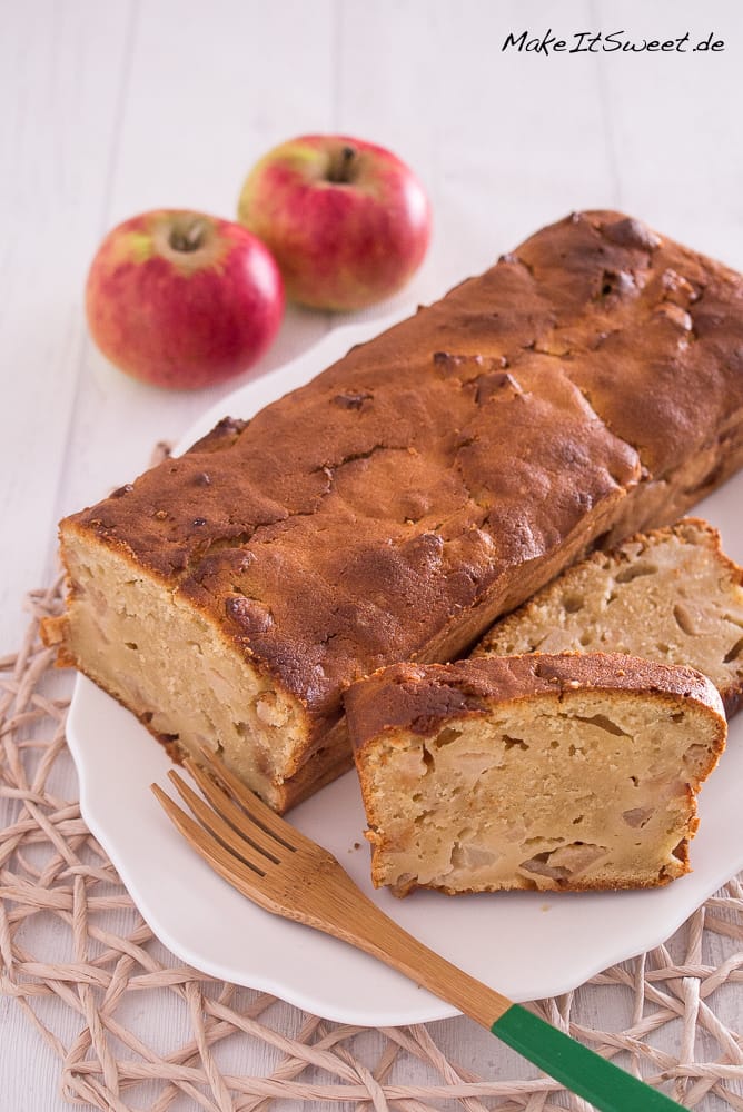 Apfel-Quark-Kuchen aus der Kastenform 1 Apfel-Quark-Kuchen aus der Kastenform mit zwei geschnittenen Scheiben, einer Holzgabel und zwei Äpfeln auf einem weißen Teller.