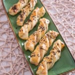 Blätterteig mit Räucherlachs Stangen Auf einem grünen, rechteckigen Teller sind sechs mit Räucherlachs gefüllte Blätterteig-Stangen angeordnet.