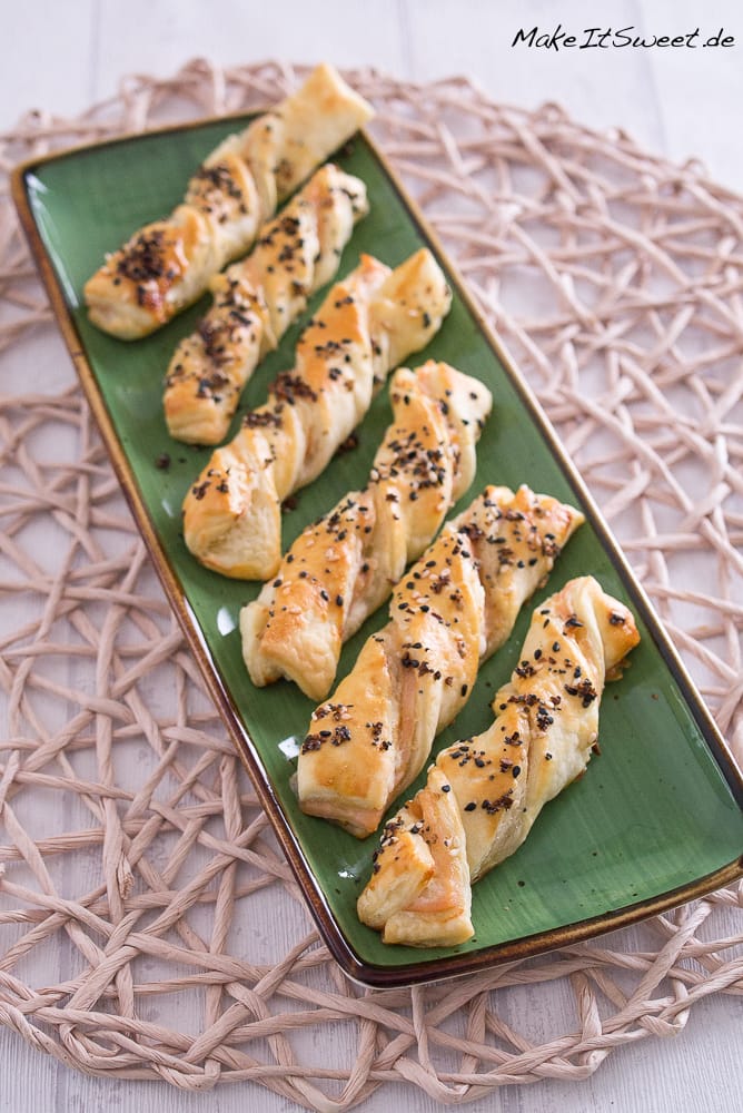 Alle Rezepte vom Foodblog MakeItSweet 1 Auf einem grünen, rechteckigen Teller sind sechs mit Räucherlachs gefüllte Blätterteig-Stangen angeordnet.