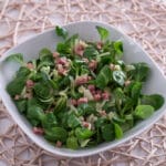 Feldsalat mit Speck in einer weißen Schale, mit frischen grünen Salatblättern und Schinkenwürfeln.