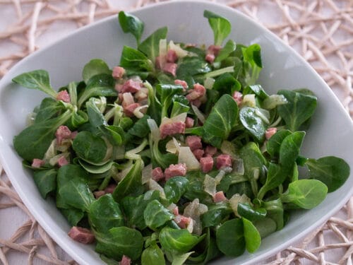 Feldsalat mit Speck in einer weißen Schale, mit frischen grünen Salatblättern und Schinkenwürfeln.