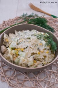 Cremiger Nudelsalat mit Hähnchen mit Mais, Gurken und Dill in einer Schüssel.