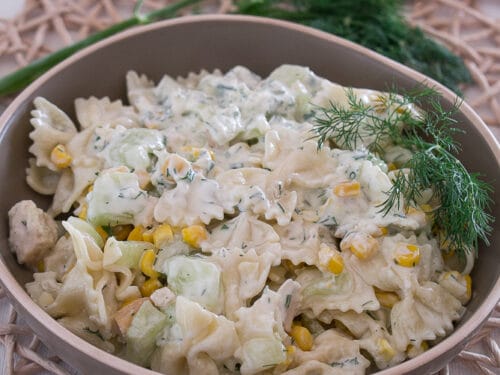 Cremiger Nudelsalat mit Hähnchen mit Mais, Gurken und Dill in einer Schüssel.