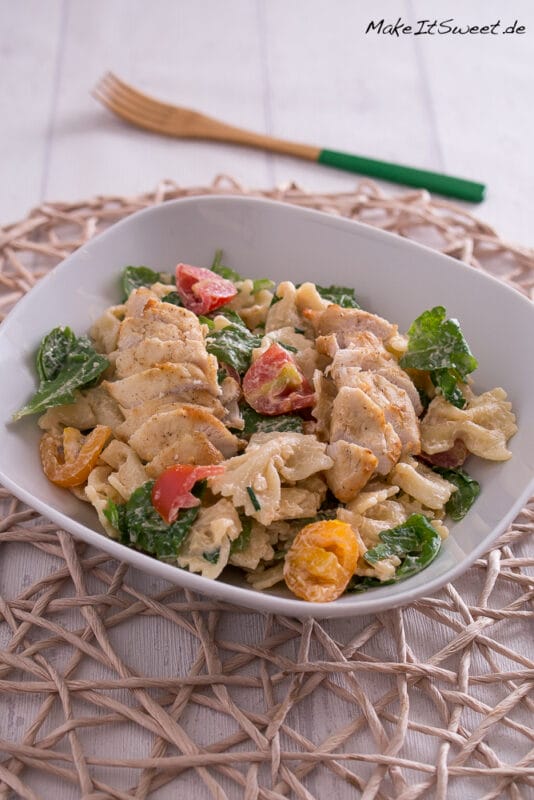 Nudelsalat mit Rucola, Hähnchen und Tomate + French-Dressing 2 Nudelsalat mit gegrilltem Hähnchen, Tomaten, Rucola und Soße, serviert in einer weißen Schale.
