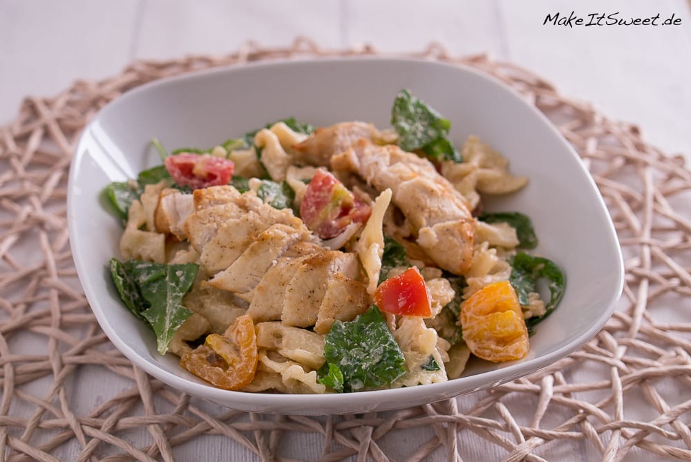 Nudelsalat mit Rucola in einer Schüssel mit gegrilltem Hähnchen, Rucola und Kirschtomaten.