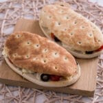 Zwei Panini-Fladenbrot-Sandwiches mit Oliven, Feta und Gemüse auf einem Holzbrett, knusprig und frisch aus einer Heißluftfritteuse.