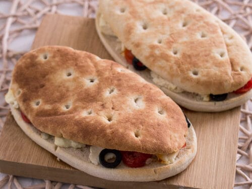Zwei Panini-Fladenbrot-Sandwiches mit Oliven, Feta und Gemüse auf einem Holzbrett, knusprig und frisch aus einer Heißluftfritteuse.
