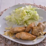 Gebratene Fleischstücke mit Zwiebeln und frischem Salat, serviert auf einem weißen Teller.