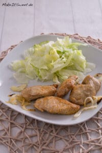 Puten Ministeaks aus der Heißluftfritteuse mit Zwiebeln 5 Gebratene Fleischstücke mit Zwiebeln und frischem Salat, serviert auf einem weißen Teller.