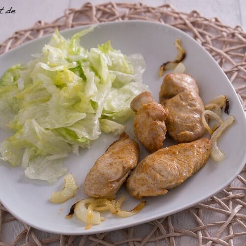 Puten Ministeaks aus der Heißluftfritteuse mit Zwiebeln 3 Blattsalat, gegrillte Fleischröllchen und sautierte Zwiebeln auf einem weißen Teller.