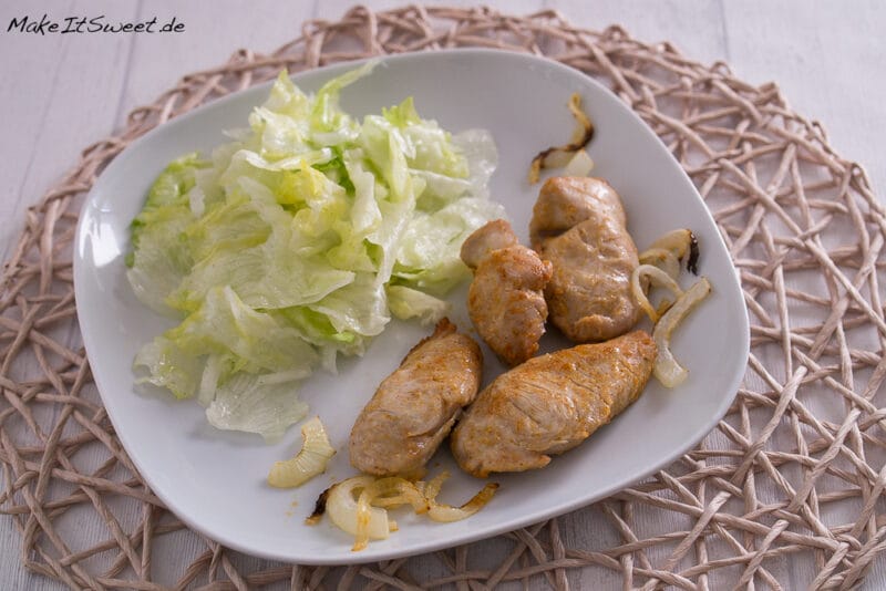 Puten Ministeaks aus der Heißluftfritteuse mit Zwiebeln 1 Blattsalat, gegrillte Fleischröllchen und sautierte Zwiebeln auf einem weißen Teller.