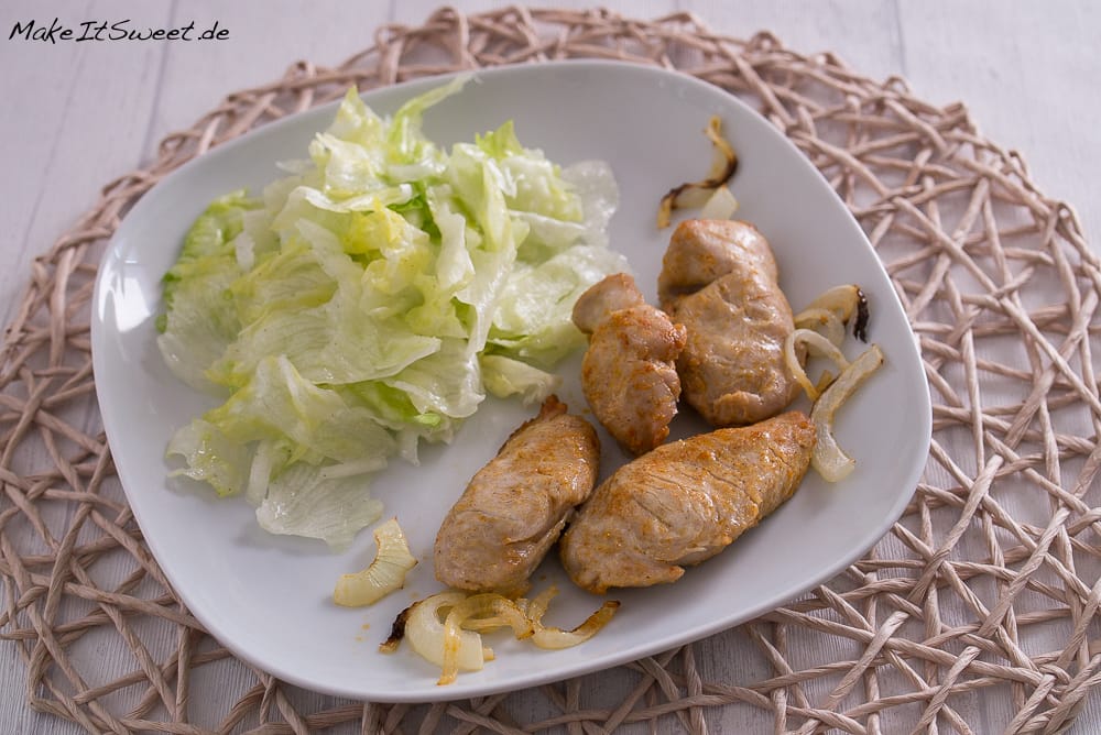 Blattsalat, gegrillte Fleischröllchen und sautierte Zwiebeln auf einem weißen Teller.