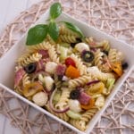 Italian Nudelsalat in einer quadratischen Schüssel mit Tomaten, Oliven, Mozzarella, Salami und Basilikum.