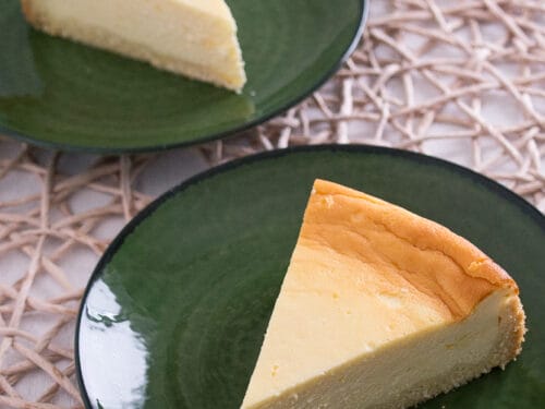 Zwei Stücke luftiger Käsekuchen auf grünen Tellern.