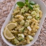 Nudelsalat mit Erbsen, Gurke, Basilikum und Zitronenscheiben auf einer weißen Platte.