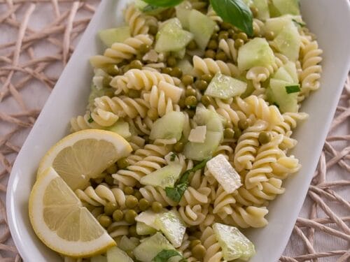 Nudelsalat mit Erbsen, Gurke, Basilikum und Zitronenscheiben auf einer weißen Platte.