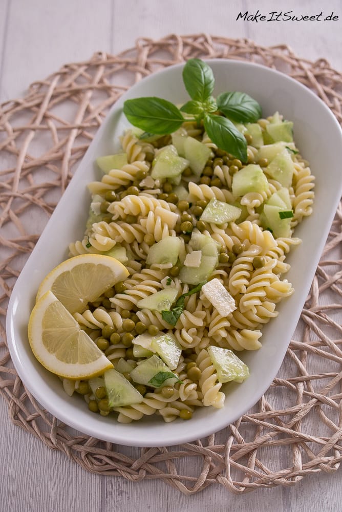 Nudelsalat mit Erbsen, Gurke, Basilikum und Zitronenscheiben auf einer weißen Platte.