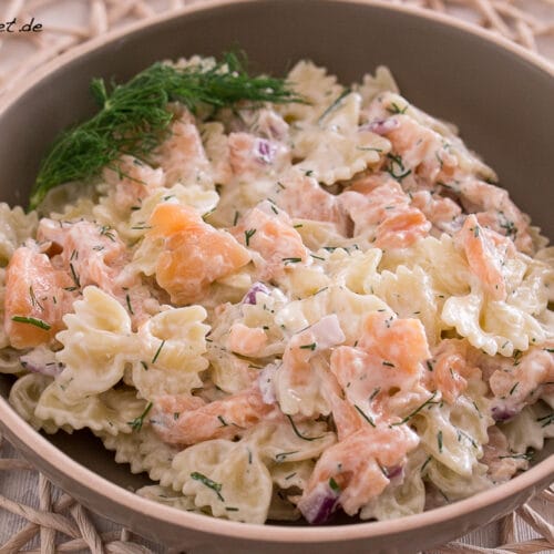 Cremiger Nudelsalat mit Räucherlachs, Dill und roten Zwiebeln in einer braunen Schüssel.
