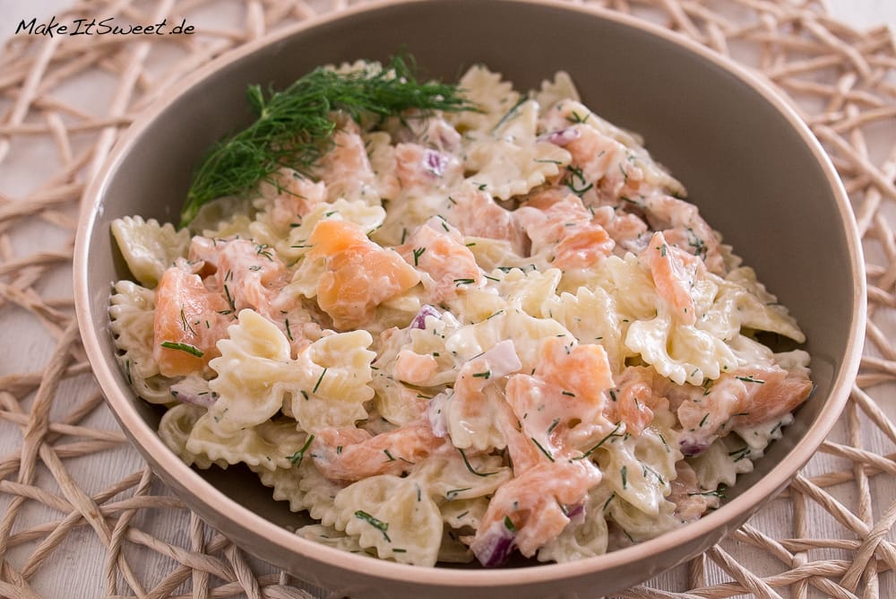 Cremiger Nudelsalat mit Räucherlachs, Dill und roten Zwiebeln in einer braunen Schüssel.