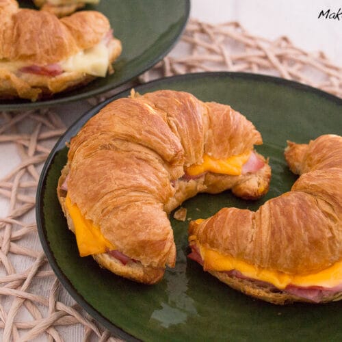Zwei Croissant mit Schinken und Käse auf dunkelgrünen Tellern.