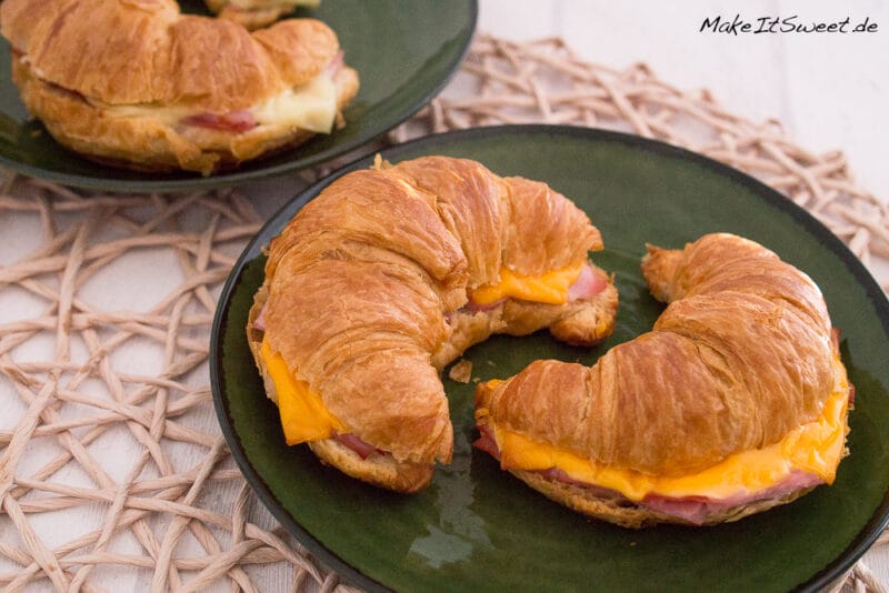 Zwei Croissant mit Schinken und Käse auf dunkelgrünen Tellern.