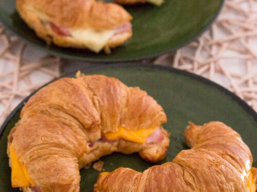 Croissant mit Schinken und Käse aus der Heißluftfritteuse auf grünen Tellern.
