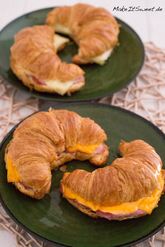 Croissant mit Schinken und Käse aus der Heißluftfritteuse auf grünen Tellern.