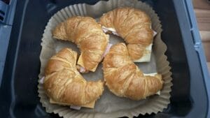 Vier mit Schinken und Käse gefüllte Croissant-Sandwiches auf Backpapier in einem Backblech.